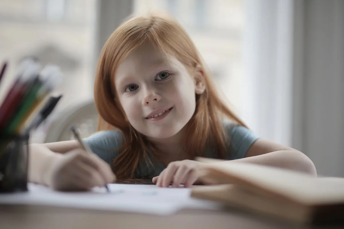 A child smiling while writing at a table